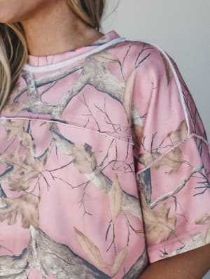 A close-up detail shot of a pink camo top with exposed seam detailing — the kind of piece that's equal parts playful and effortless, like you meant to be this fun.