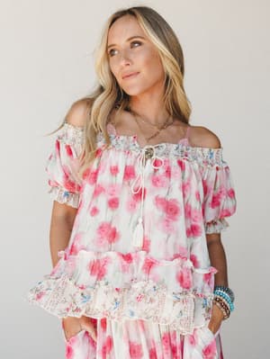 A flowy off-shoulder floral top in soft pink and white is styled as a set with a matching skirt, layered with boho jewelry — the kind of outfit that feels like a garden party you actually want to go to.