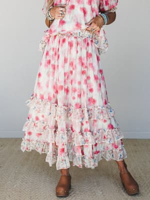 A flowy floral maxi skirt with tiered ruffle hem is styled with a matching top and stacked boho jewelry — the kind of outfit that feels like a garden party and a road trip at the same time.