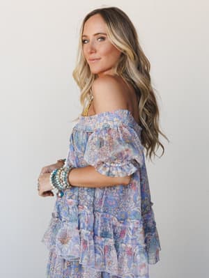 A flowy off-the-shoulder top in a dreamy periwinkle and pink floral print, styled with stacked boho bracelets — the kind of outfit that feels effortless but totally intentional.