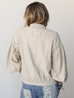A back-view shot of a model in a relaxed cream button-down sweater with voluminous balloon sleeves and a center back seam detail, paired with acid wash jeans featuring floral patchwork pockets — effortlessly lived-in and easy.
