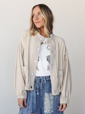 A relaxed, layered look built around a cream mixed-media jacket with ribbed knit front panels and snap buttons, worn open over a white tiger-print tee and acid wash wide-leg denim — the kind of outfit that looks effortless but was absolutely thought