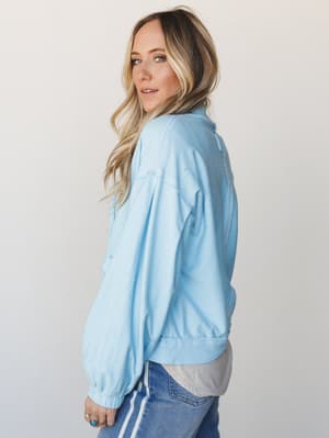 A relaxed side-profile shot of a light blue button-down sweater with a lived-in, soft feel — styled over a grey layer with blue jeans for an effortlessly cozy everyday look.