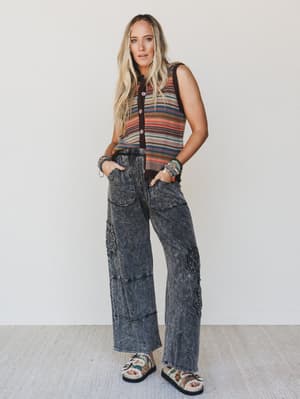 Woman wearing a sleeveless striped top and wide-leg jeans against a white background