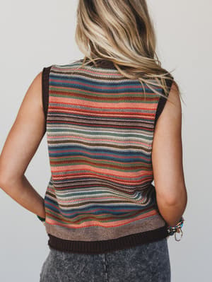 Person wearing a multicolored striped sleeveless sweater against a plain background