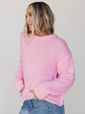 Woman wearing a pink sweater and blue jeans against a plain background