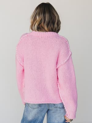 Person wearing a pink knitted sweater and blue jeans on a plain background