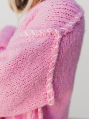 Close-up of a pink knitted garment with white stitching detail.
