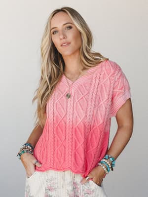 A coral cable-knit short sleeve sweater top styled with floral wide-leg pants and stacked boho bracelets — the kind of outfit that looks equally at home on a beach boardwalk or a Saturday brunch patio.
