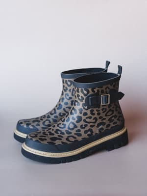 A pair of short rubber rain boots in a bold leopard print with a chunky lug sole and side buckle detail — the kind of boots that make a rainy day feel like a choice.