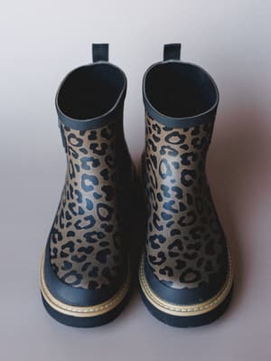 A pair of leopard-print rubber rain boots shot from above against a soft gray studio background — the kind of boots that make a rainy Tuesday feel like a personal style moment.