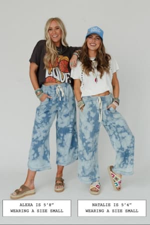 Two women wear The Nest So Comfy Wide Leg Denim Pant in Bleach Dye Denim with casual tops, smiling side by side. Both are in size small; one is 5'8" and the other 5'4", as shown by height labels below their feet.