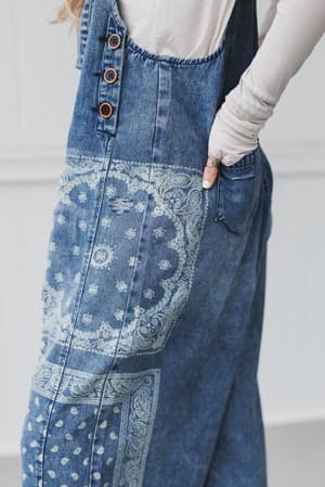 Wearing the High Hopes Slouchy Denim Overalls in Denim Bandana with a white long-sleeve shirt, one hand in the side pocket; only the lower half of the body is shown.