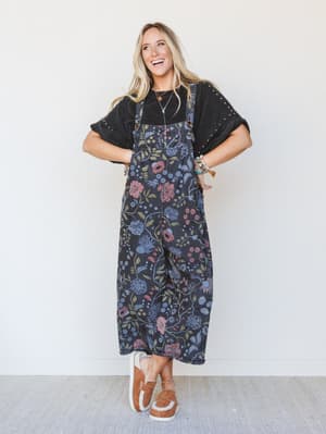 Woman wearing a floral overalls and black top against a white background