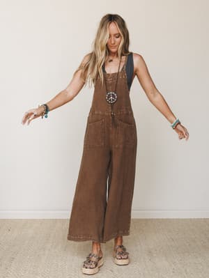A wide-leg waffle-texture overall in warm chocolate brown, styled over a black tank with layered boho jewelry and espadrille platform sandals — effortless and a little 70s, in the best way.
