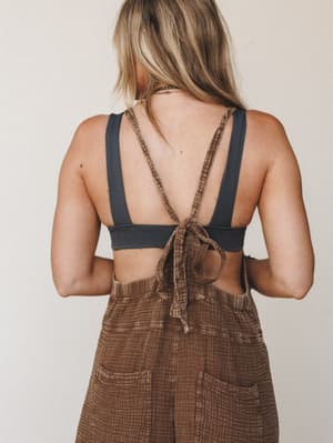 Shot from behind, this look pairs a charcoal bralette with chocolate brown textured overalls that tie across the back — the kind of effortless outfit that somehow looks totally intentional.