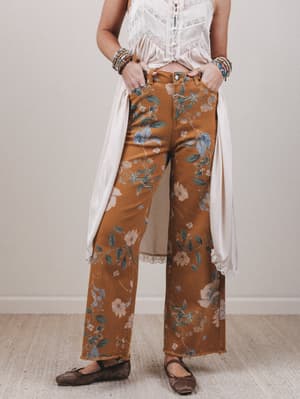 Person wearing brown floral pants with a white top and brown shoes on a plain background