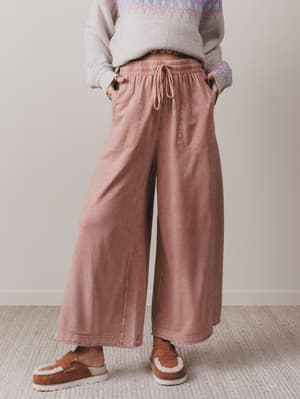 Person wearing pink wide-leg pants and a patterned sweater in a neutral setting