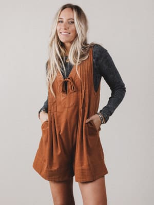 Woman wearing a brown corduroy romper over a dark long-sleeve shirt against a plain background