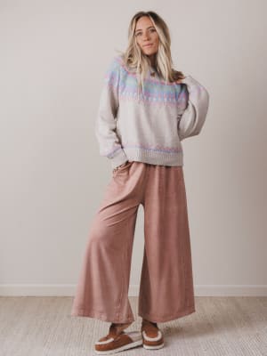 Woman wearing a patterned sweater and wide-leg pants against a plain background