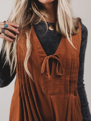 Person wearing a brown corduroy dress over a black top with a neutral background