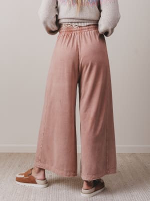 Person wearing pink wide-leg pants and a patterned sweater against a plain background