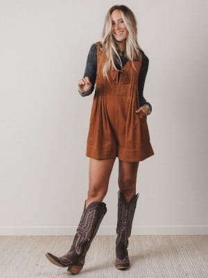 Woman wearing a brown suede dress and cowboy boots against a plain background