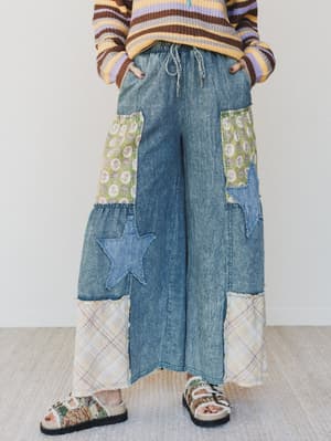 Person wearing a colorful sweater and patchwork jeans with floral and star patterns on a white background.