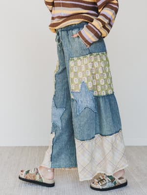 Person wearing a colorful sweater and patchwork pants with a white background