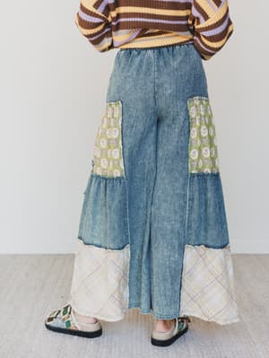 Person wearing a brown and yellow striped sweater with a blue denim skirt featuring patterned patches on a light gray background.