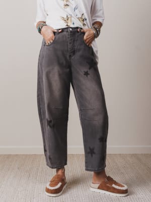 Person wearing gray acid-wash jeans with star patterns and brown slip-on shoes on a neutral background.