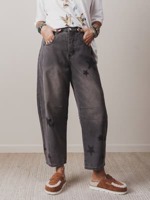 Person wearing gray acid-wash jeans with star patterns and brown slip-on shoes on a neutral background.