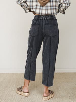 Shot from behind, a model wears acid-washed black barrel-leg pants with a smocked elastic waist and patch pockets, styled with a plaid flannel and leopard print platform espadrilles for an effortlessly relaxed, lived-in look.