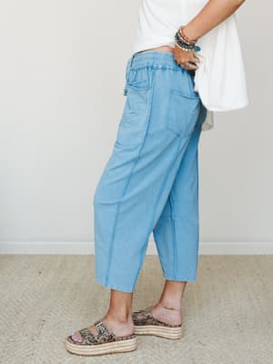 A side-profile shot of relaxed barrel-leg crop pants in a soft washed blue, styled with a white tee, leopard print platform sandals, and a stack of boho bracelets — the kind of outfit that looks effortless but was definitely thought about.