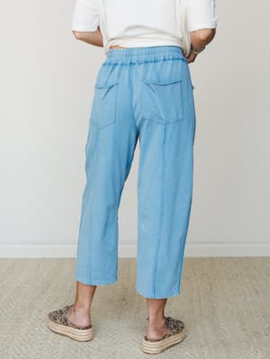 Shot from the back, these light blue barrel-leg pants have an easy, lived-in feel — smocked waistband, patch pockets, and a relaxed cropped silhouette styled with a white tee and leopard platform espadrilles.