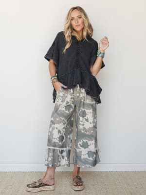 A relaxed full-body shot of a model in a washed black ruffle top and wide-leg tie-dye cropped pants, styled with turquoise stacked bracelets and espadrille platform sandals — effortlessly boho with just the right amount of 'I didn't try that hard.'