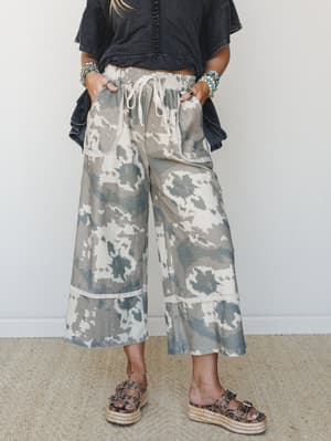 Wide-leg cropped pants in a soft camo-meets-tie-dye print styled with a washed black tiered top and platform espadrille sandals — the kind of effortless, lived-in outfit that looks like it came together without trying.