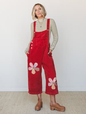 Red corduroy wide-leg overalls with patchwork floral appliqués styled over an olive striped turtleneck and worn with tan platform clogs — the kind of outfit that looks effortless but clearly took thought.