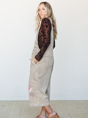A relaxed side-profile shot of a model in slouchy corduroy overalls layered over a floral velvet mesh long-sleeve — the kind of outfit that looks effortless but clearly had a thought behind it.