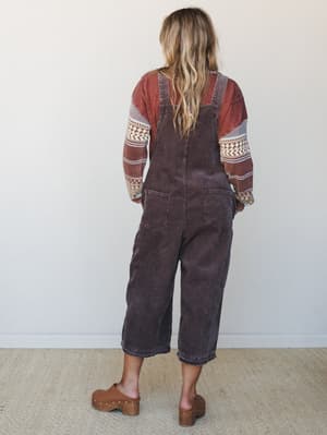 Shot from behind, a model in wide-leg corduroy overalls layered over a patterned rust sweater with clogs — an easy fall outfit that feels pulled-together without trying.