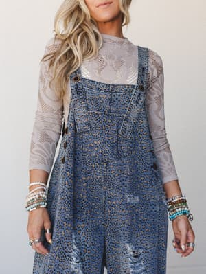 A leopard-print denim overall layered over a soft lace long-sleeve top, styled with stacks of beaded bracelets and rings — the kind of outfit that looks like it came together effortlessly but definitely didn't.