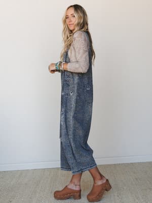 A relaxed, lived-in look featuring wide-leg leopard-print denim overalls layered over a floral lace long-sleeve top, styled with tan clogs and stacked beaded bracelets — the kind of outfit that feels effortless but clearly wasn't an accident.