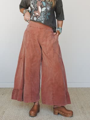 Wide-leg pants in a washed brick tone styled with a faded graphic tee, wood-platform clogs, and stacked turquoise jewelry — the kind of outfit that looks effortless but was absolutely thought about.