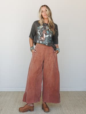 A relaxed, earthy outfit pairing wide-leg brick pants with a faded graphic tee and wood clogs — the kind of put-together-but-effortless look that feels like it was assembled in five minutes and took zero stress.