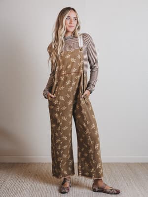 Woman wearing a brown patterned jumpsuit with a striped shirt underneath against a plain background