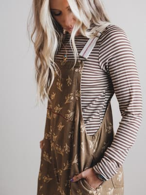 Woman wearing a striped long-sleeve shirt and patterned overalls against a plain background
