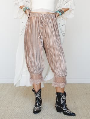 Pleated velvet-texture jogger pants in a warm mocha stripe, finished with a lace hem and paired with embroidered black cowboy boots and a white sequin kimono — the kind of outfit that somehow works perfectly and you can't fully explain why.