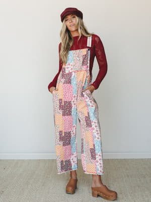 A wide-leg patchwork floral overall jumpsuit styled with a burgundy crochet long-sleeve top, baker boy cap, and tan clogs — the kind of outfit that looks like it was pulled together effortlessly but definitely wasn't.