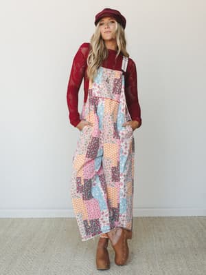 A patchwork floral wide-leg jumpsuit layered over a crimson lace top, styled with a newsboy cap and studded ankle boots — the kind of outfit that looks like it was pulled together effortlessly but absolutely was not.