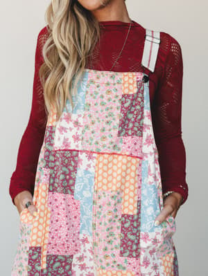 A patchwork floral overall dress layered over a deep red lace long-sleeve top — the kind of outfit that looks like it was pulled together effortlessly but definitely wasn't.